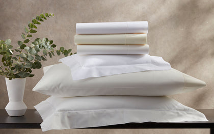 White and ivory Luca Hemstitch sheets stacked with hemstitch trim, beside a eucalyptus sprig.