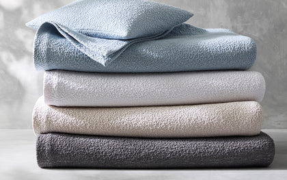 Malibu textured bouclé bedding stacked in blue, gray, tan, and charcoal.