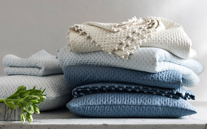 Margaret textured quilted bedding with pompom trim, stacked in ivory and shades of blue.