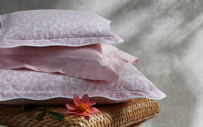 Pink Margot vine-print scalloped bedding stacked on a woven bench.