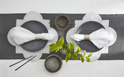 Gray scalloped-edge placemats set on a table runner with dark plates and greenery.