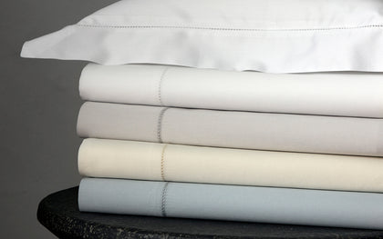 Nocturne Hemstitch sheets stacked in assorted colors on a stone stool with a berry sprig on top.