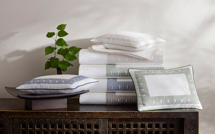 White Ophelia Pique bedding with Greek key trim in assorted colors stacked on a carved wood console.