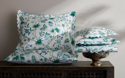 White Palmyra floral-print pillows with scalloped edges stacked on a carved dark console.