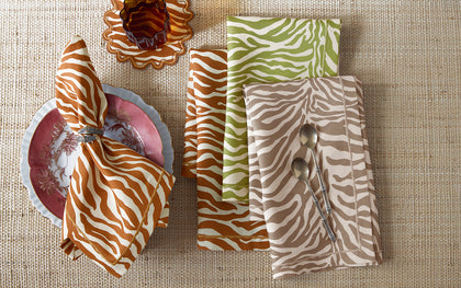 Zebra-print Regine napkins in orange, green, and tan set on a woven placemat with floral china.