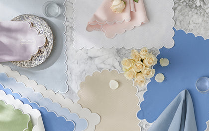 Scalloped-edge Savannah Gardens placemats and napkins in pastel colors on marble with white roses.