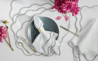 White Scallop Edge placemats and napkins with gray wavy trim, styled with pink dahlias and a dark plate.