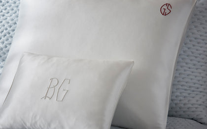 White silk monogrammed pillows from The Silk Collection styled on a quilted bed.