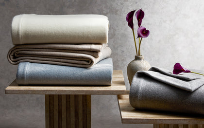 Venus wool blankets folded in assorted colors on wood stands beside purple calla lilies.