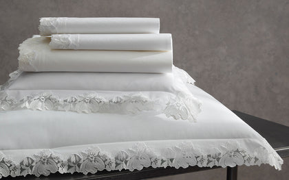White Virginia bedding with floral lace trim stacked on a dark table.
