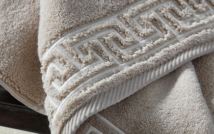 Tan Adelphi towel with textured greek-key trim, folded.
