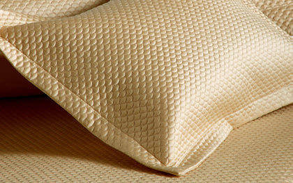 Gold Alba textured pique pillow shown in detail on matching bedding.