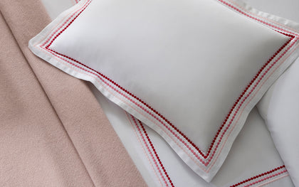 White Amara Triple Pearl pillow with red and pink dot-embroidered trim, shown in detail.