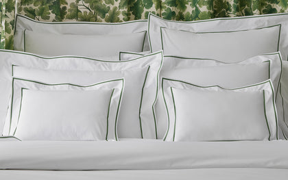 White Ansonia shams with green single-stripe trim, piled on a bed.