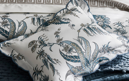 Blue Apolline floral print scalloped pillows on a blue quilted bed.