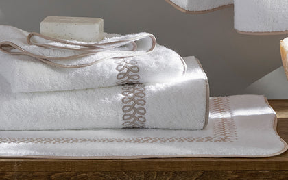 White Astor Braid towels with tan loop-embroidered trim, folded beside a bar of soap.