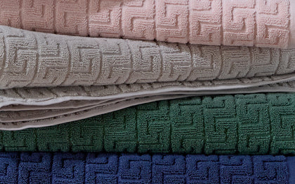 Stack of Athena towels in pink, tan, green, and navy Greek key weave