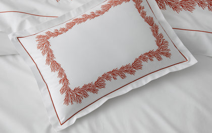 White Atoll pillow with coral-branch embroidered border, styled on a bed.