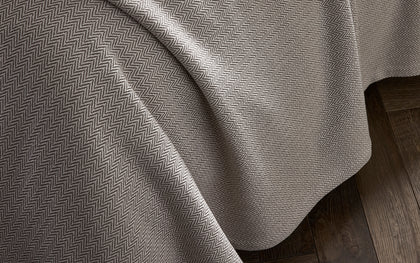 Tan Avalon herringbone-woven blanket draped over a bed.