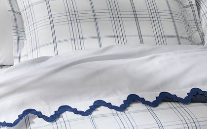 White Aziza bedding with navy wavy trim, styled with plaid pillow shams on top.