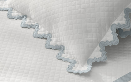 White Aziza Matelasse quilted pillow with blue wavy trim.