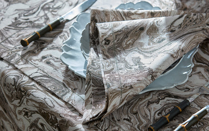 Brown Balthazar marbled-print tablecloth set with scalloped plates and dark handled flatware.