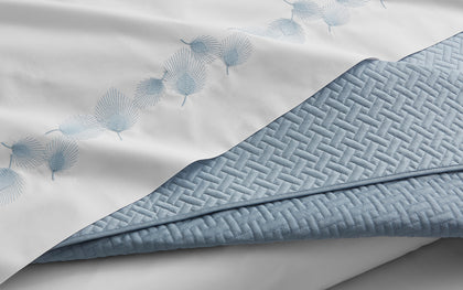 Blue Basketweave quilted blanket folded back over white sheets with fan-embroidered trim.