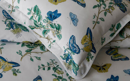 White pillow sham in the Baudin Butterfly print with blue and gold butterflies and flanged edge.