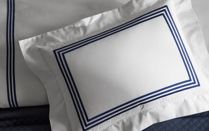 White Bel Tempo pillow with navy triple-stripe trim, styled on a navy quilted bed.