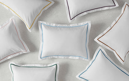 White Bergamo pillows with single-stripe trim in assorted colors, arranged flat.