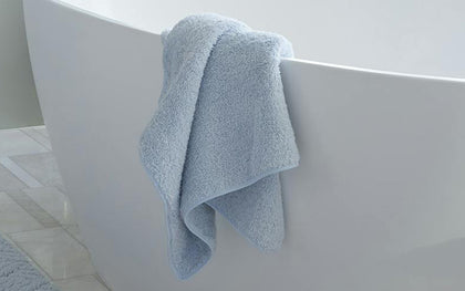 Pale blue Cairo towel draped over the edge of a soaking tub.