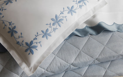 Blue Callista floral vine embroidered pillow, shown in detail on a speckled quilted bed.