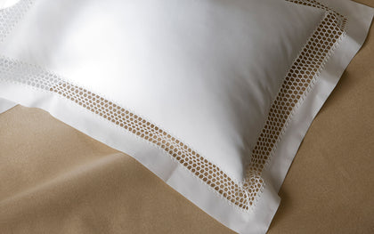 White Cecily pillow with lattice lace trim, styled on tan bedding.