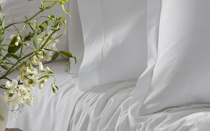 White Ceylon Satin Stitch bedding styled on a bed with white sweet pea flowers.