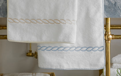 White Classic Chain towels with tan and blue chain-link trim, hung on a brass towel rack.