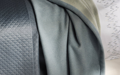 Slate blue Cosmo blanket draped over quilted bedding.