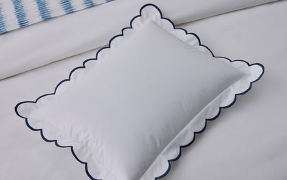 White Dakota scalloped pillow with navy trim, styled on a bed.