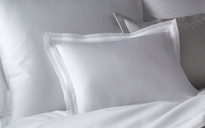 White Grace pillows with lace trimmed borders against a herringbone quilted headboard.