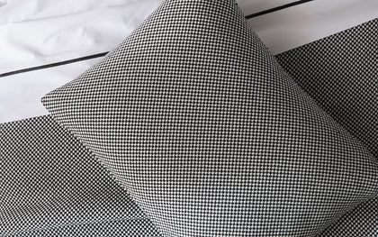Black and white Jackson houndstooth-textured pillow, layered on a bed with matching sheets.