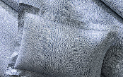 Blue-gray Jasper pebbled print pillows, layered on a bed.