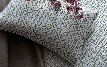 Green Laksha medallion print pillow, layered on a bed with purple orchids.