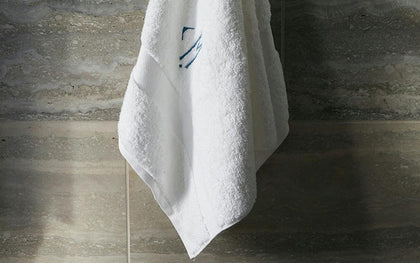 White monogrammed Lotus towel hanging on a marble tile wall.