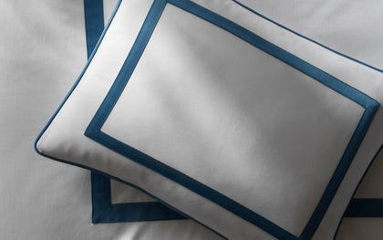 White Louise pillow with a blue bordered trim, layered on a bed.