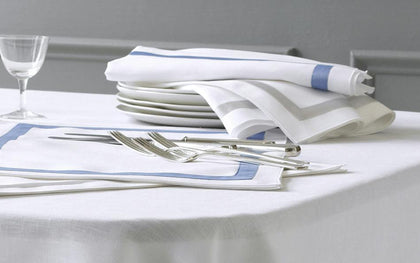 White Lowell napkins with blue and gray bordered trim, set with white plates and a wine glass.