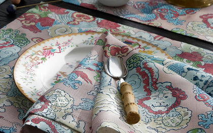 Pink Magic Mountain dragon print placemat and napkin, set with a floral plate and bamboo-handled spoon.