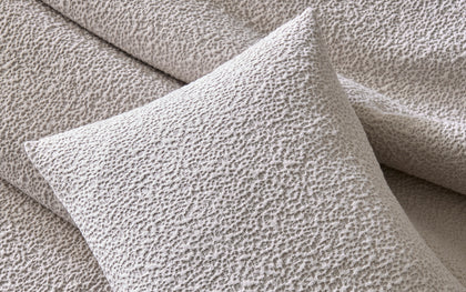 Ivory Malibu textured bouclé pillow, layered on a bed.