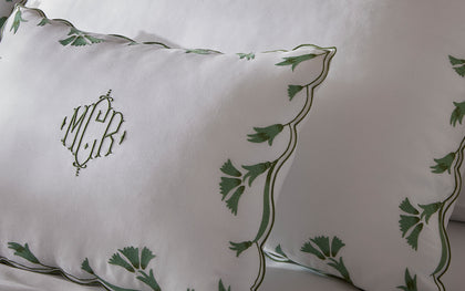 White monogrammed Marcella pillows with a green vine-embroidered scalloped border.