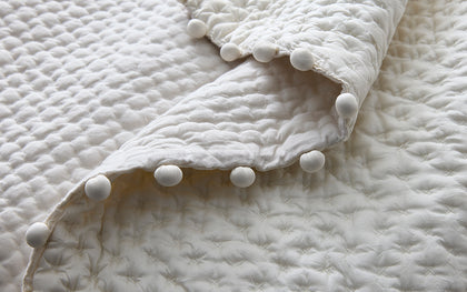Ivory Margaret textured quilted bedding with a pompom trim edge.