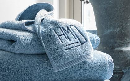 Blue Milagro towels stacked with a monogrammed washcloth draped over the top.