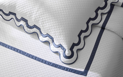 White diamond-quilted Mirasol Matelasse coverlet with scalloped navy trim on a bed.